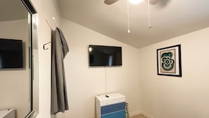 Une chambre à coucher avec un lit, un ventilateur de plafond, une télévision, une commode et un tableau encadré au mur.