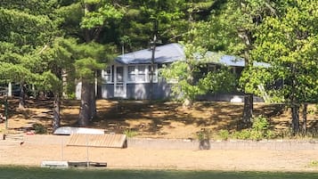 Surrounded by lush greenery, this lakeside cabin offers a serene retreat with a small porch and a sandy beach at its doorstep.