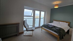 Una camera da letto con un letto, una sedia, un termosifone e vista attraverso un'ampia finestra.