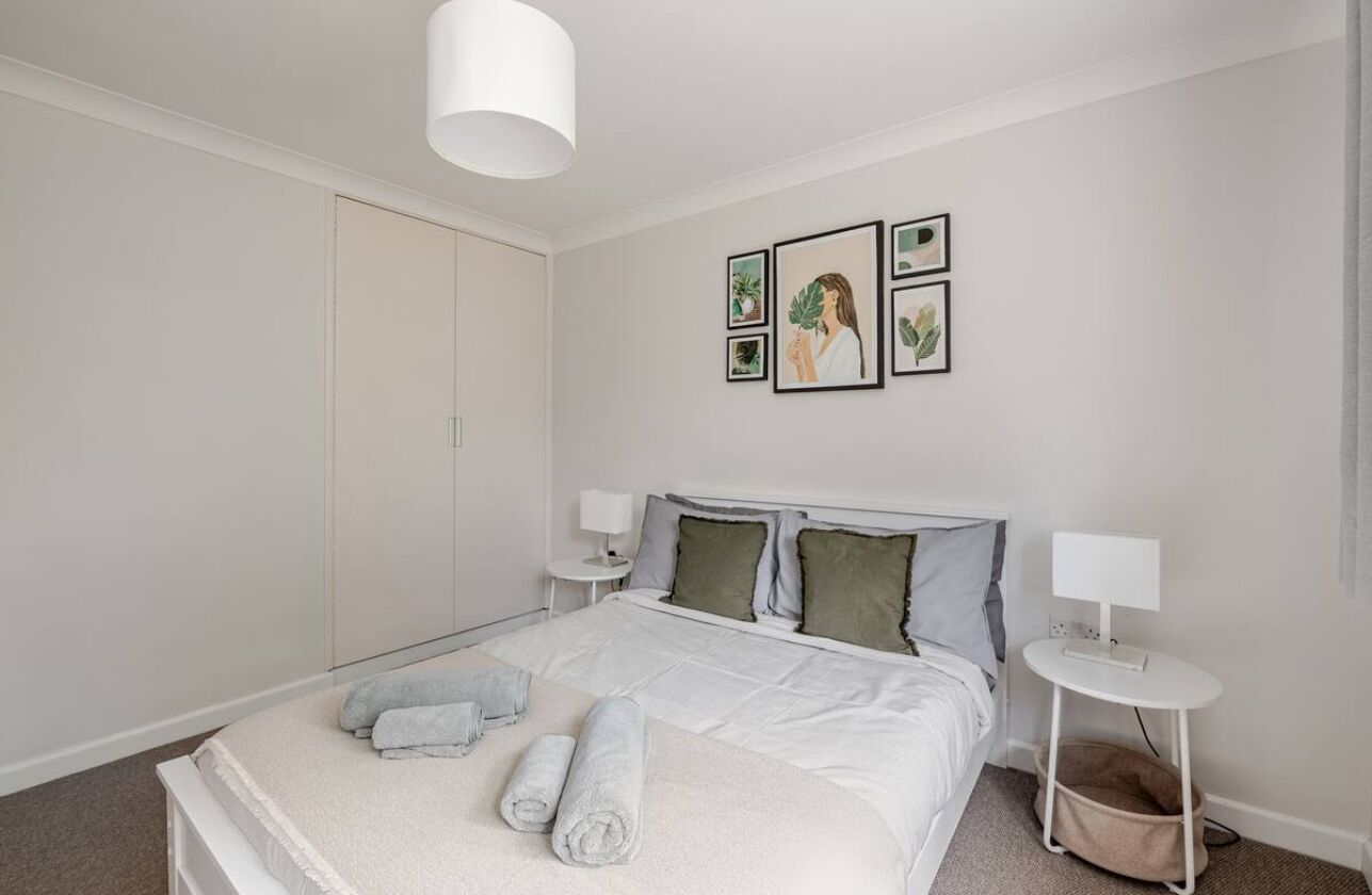 A neatly arranged bedroom with a bed, pillows, a bedside table, and a wall-mounted lamp.