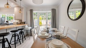 A dining area with a wooden table set for four, white chairs, and a bar area with stools.