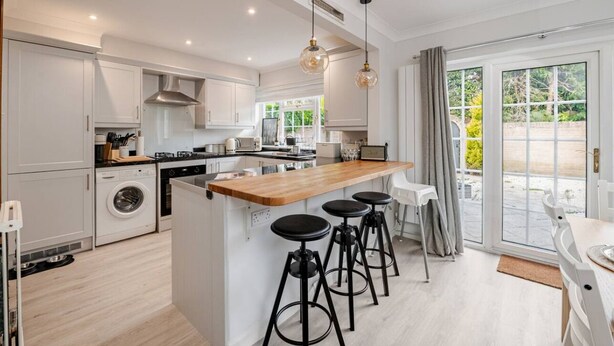 A modern kitchen with a central island, bar stools, and a view to the outside.