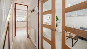 A modern interior with a wooden door, a view into a room with a plant, and a glimpse of a kitchen area.