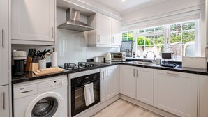 A modern kitchen with white cabinets, a built-in washing machine, a stove, and a window providing a view of greenery outside.