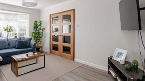 A modern living room with a blue sofa, a wooden coffee table, and a large wooden door with glass panels.