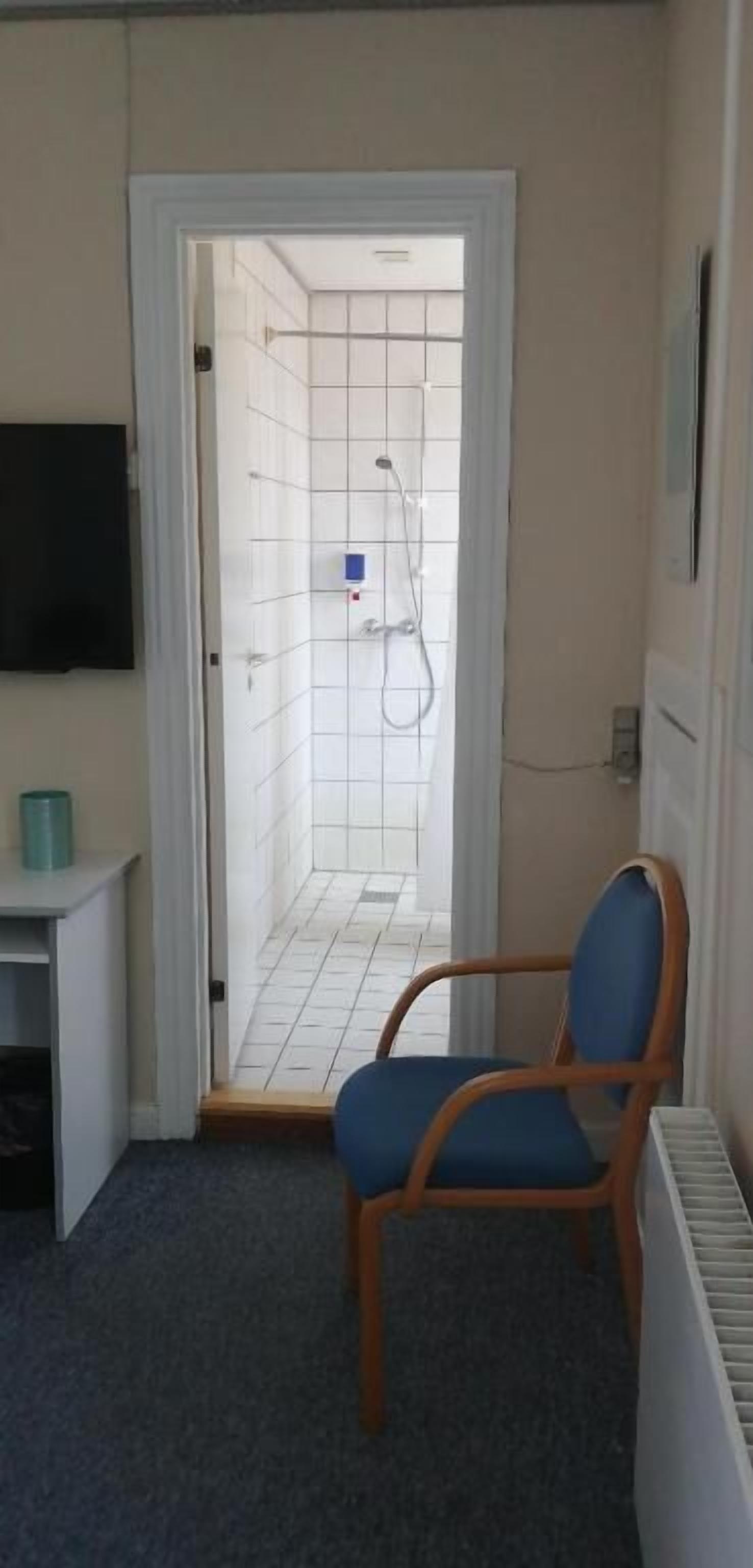 Ett badrum med dusch, en stol, ett litet bord och ett element.