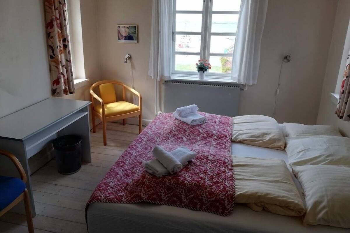A bedroom with a bed, a chair, a desk, and a window with a view.