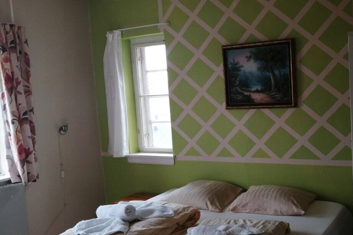 A room with a bed, a window, a painting, and a bunk bed.