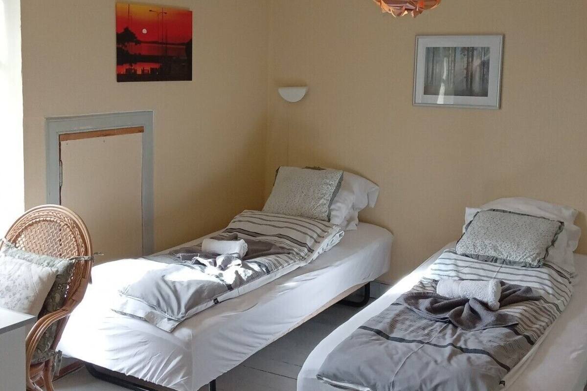 A room with two single beds, a desk, a chair, and a hanging light fixture.