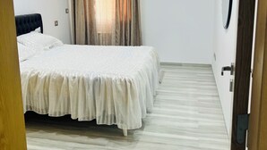 A hotel room with a large bed, a wooden floor, a window with curtains, and a round mirror on the wall. - Tranquil Mrezga Getaway: Near Beach & Hammamet Fun (Mrezga)