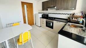 A compact kitchen with a dining area, featuring a white table, yellow chairs, a white refrigerator, a stove, and a sink with a dish rack. - Tranquil Mrezga Getaway: Near Beach & Hammamet Fun (Mrezga)