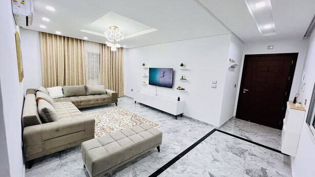 A modern living room with a sectional sofa, a coffee table, a TV, and a white entertainment unit. - Tranquil Mrezga Getaway: Near Beach & Hammamet Fun (Mrezga)