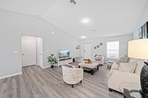 A spacious living room with a high ceiling, a television, a sofa, a coffee table, and a potted plant.