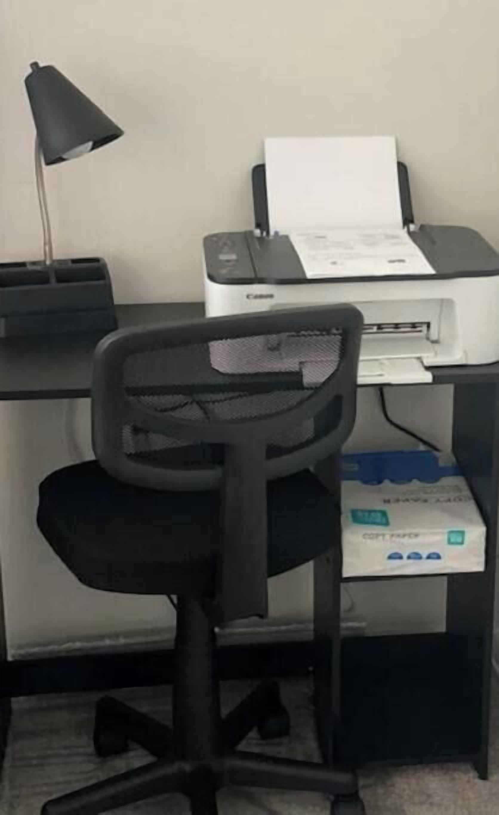 A desk with a printer, a black office chair, and a desk lamp.