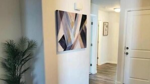 A hallway with wooden flooring, a potted plant, and a framed abstract painting on the wall. - New Home w/Patio near Laughlin/Mohave/Colorado Riv (Bullhead City)