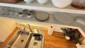 Una cocina con un lavamanos, un escurreplatos y varios cuencos y platos blancos en estantes.