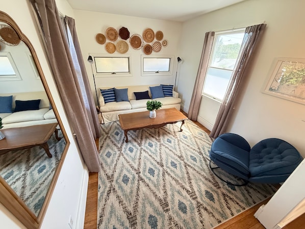 Ein Wohnzimmer mit Sofa, Couchtisch, gemustertem Teppich, blauem Sessel und Wanddekoration.