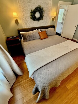 Un lit double avec une couvre-lit matelassé, deux lampes de chevet, une table de chevet avec un clavier, une guirlande décorative accrochée au mur et une porte sur la droite.