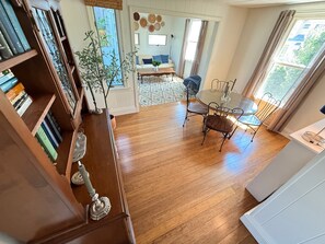 Une pièce avec un plancher en bois, une table à manger avec des chaises, une bibliothèque et une fenêtre avec des rideaux.