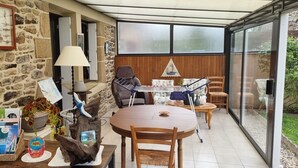 A cozy patio area with a stone wall, a wooden table, chairs, and a glass door leading to a garden. - KERYVONNE, FAMILY HOME (Sarzeau)