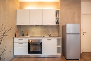 A modern kitchen with white cabinetry, a built-in oven, a stainless steel refrigerator, and a small shelf with books. - 731A Apartment Aurora (Merano)