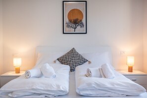 A hotel room with two beds, a large pillow, two bedside lamps, and a framed artwork on the wall. - 731A Apartment Aurora (Merano)