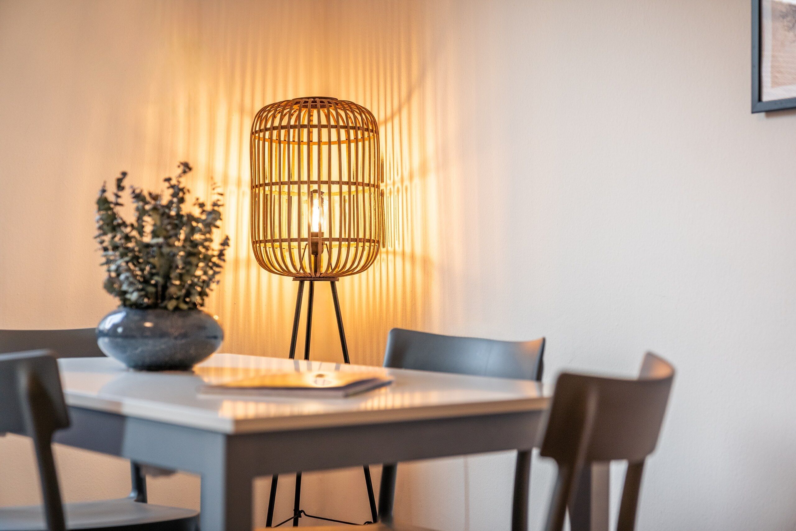 A dining area with a table, chairs, a vase with plants, and a floor lamp.