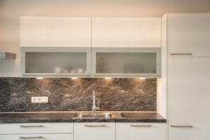 A modern kitchen with a marble countertop, a stainless steel sink, and white cabinetry. - 733B Apartment Villa Laurin (Caldaro sulla strada del vino)
