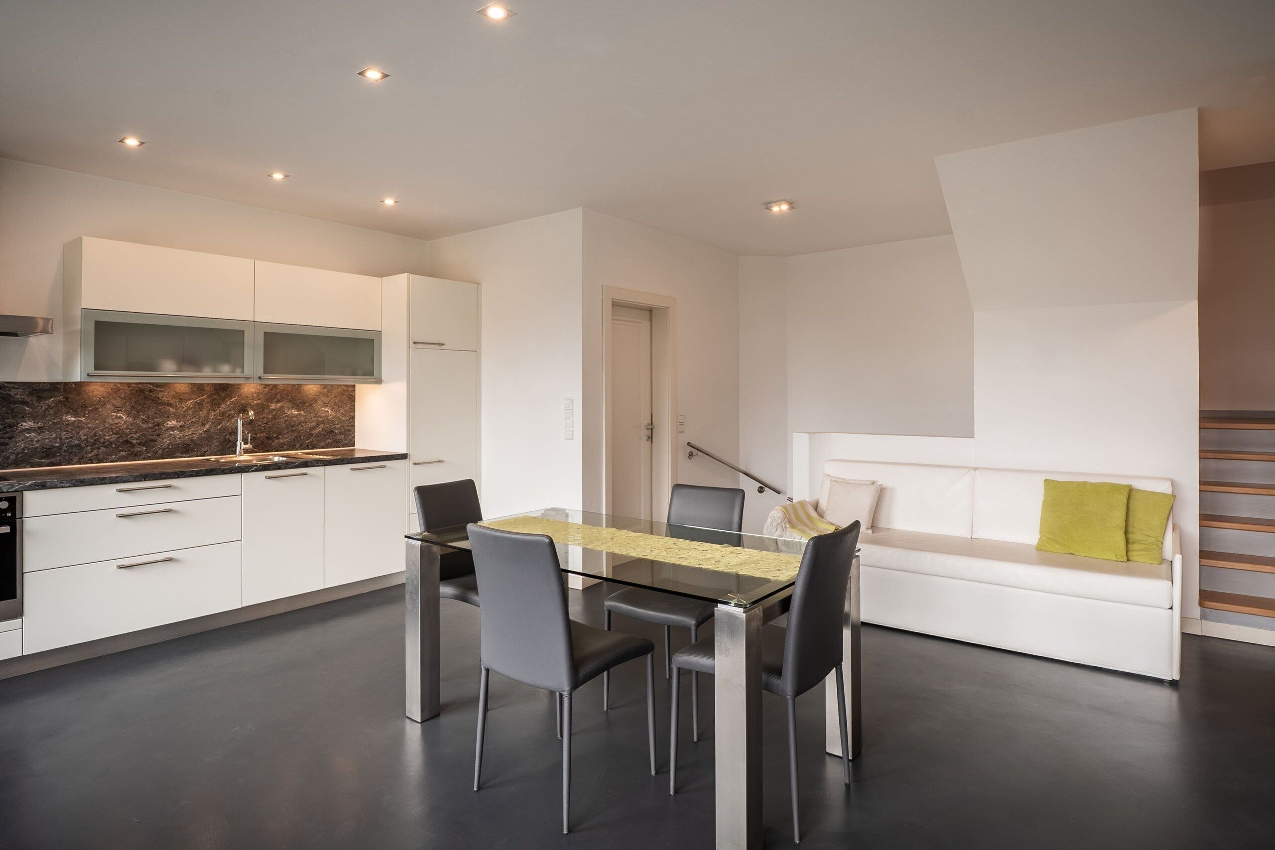 Une cuisine moderne avec des meubles blancs, un plan de travail en marbre et un coin repas comprenant une table et des chaises en verre.