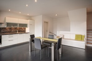 A modern kitchen with white cabinets, a marble countertop, and a dining area with a glass table and chairs. - 733B Apartment Villa Laurin (Caldaro sulla strada del vino)