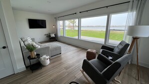 A modern living room with a sofa, chairs, a TV, and large windows overlooking a grassy area. - Newer build 3-bedroom cottage on peaceful Fremont Lake with AC, WiFi (Fremont)