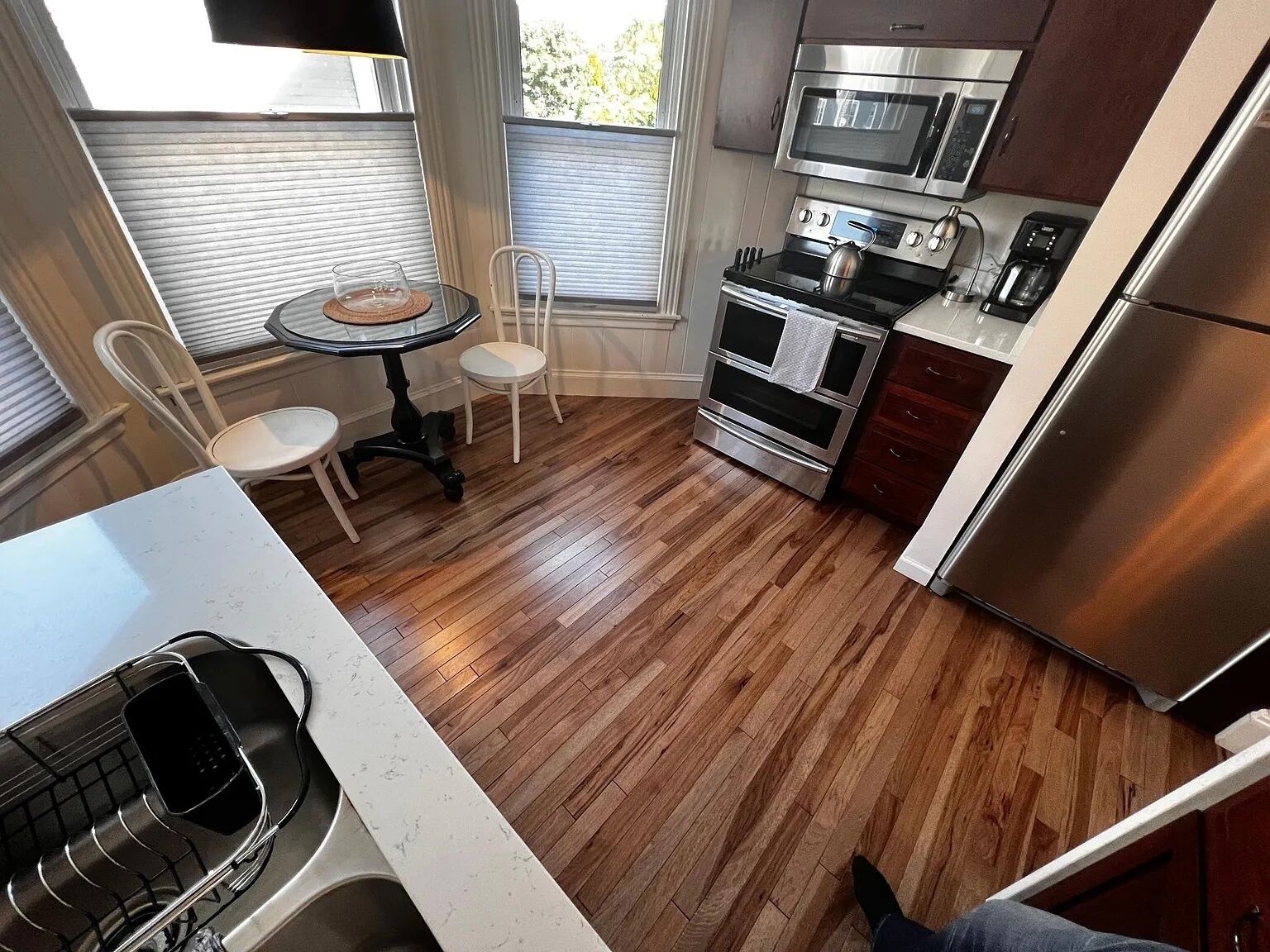 Uma cozinha com piso de madeira, uma mesa de jantar com cadeiras, uma geladeira de aço inoxidável e um forno embutido.
