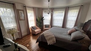 Un dormitorio con una cama grande, dos sillones, una araña de cristal y vistas al exterior.