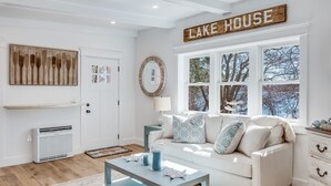 A living room with a white sofa, a coffee table, a fireplace, and a large window with a view of trees.
