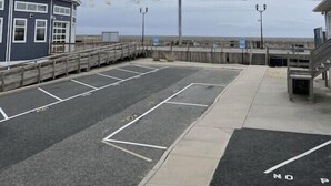 A parking area with marked spaces, a wooden walkway, and a building with a blue facade. - Oceanfront charming 2 bedroom 30 second walk to the beach (Seaside Heights)