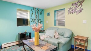A living room with a teal wall, a light green couch, a small table with a vase, and a window with blinds. - Oceanfront charming 2 bedroom 30 second walk to the beach (Seaside Heights)