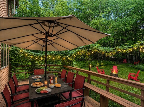 An outdoor deck with a table set for a meal, surrounded by red chairs, and a large umbrella providing shade.