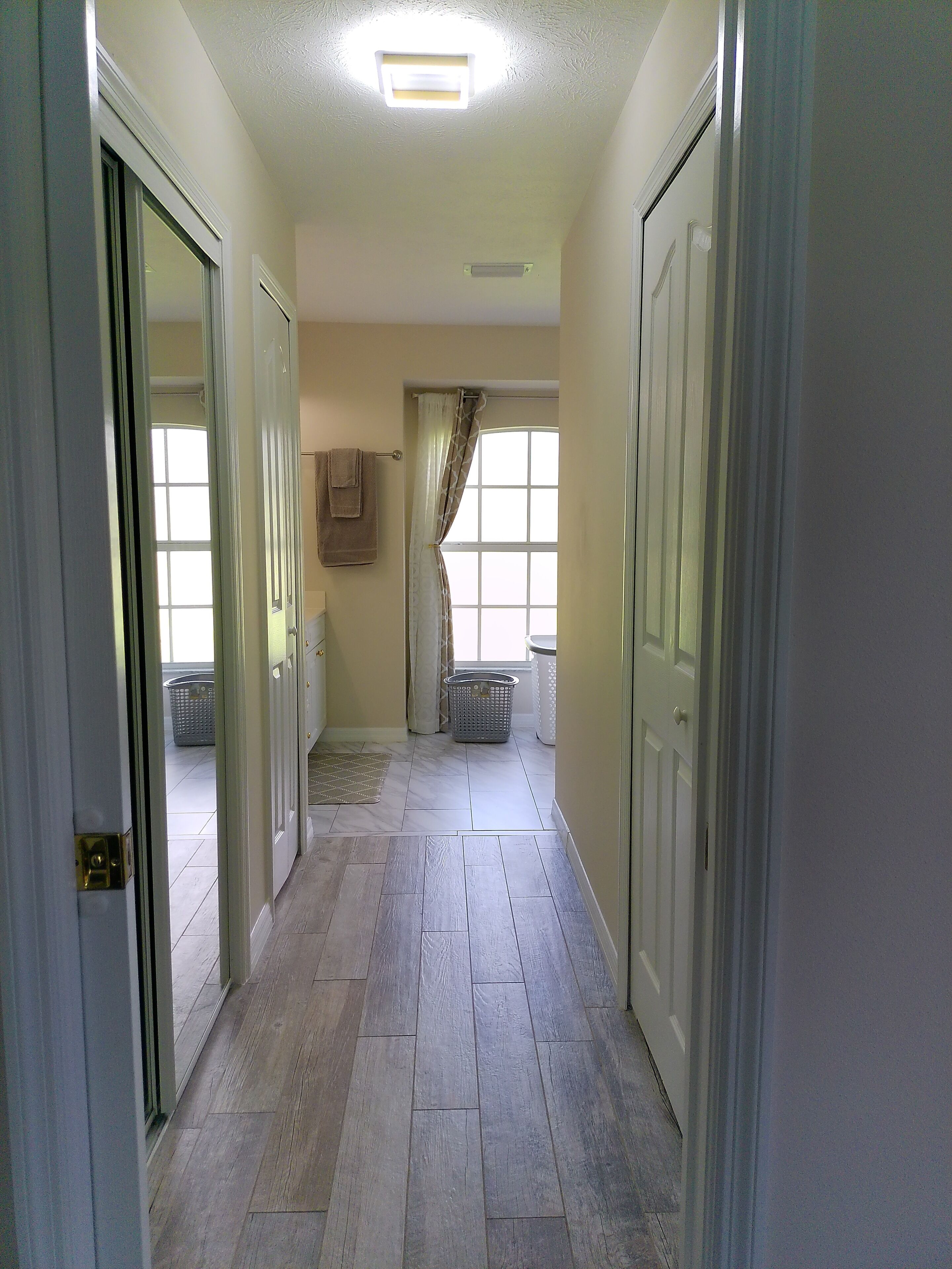 A hallway with a tiled floor, a ceiling light, a window with curtains, and a laundry basket.