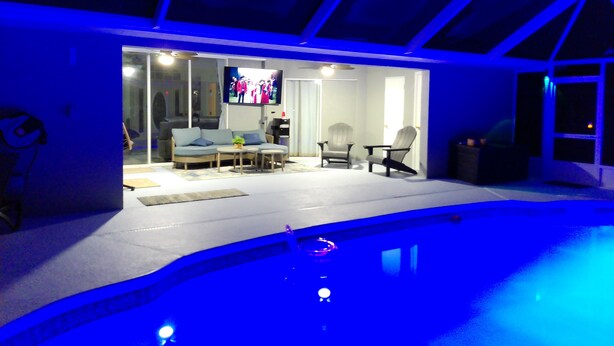 A modern indoor pool area with a glass enclosure, a seating area with a sofa and chairs, and a television screen. - Villa Varona, Private Heated Pool Included- No extra fee (Lake Placid)