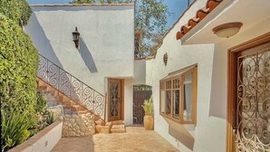 Un patio con una escalera de piedra, un muro blanco y una reja de metal.