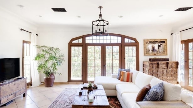 Un salón amplio con un gran ventanal, un sofá blanco, una mesa de centro de madera y un televisor sobre un mueble de madera.