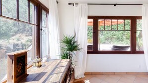 Una habitación con ventanas amplias, una mesa de madera con una vela y un adorno, además de una planta en maceta.