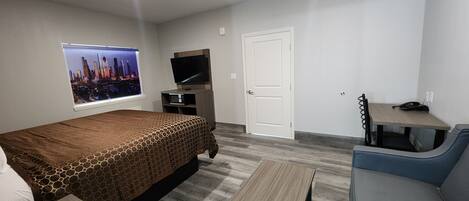 Ett hotellrum med en säng, ett skrivbord, en stol, en tv och ett fönster med utsikt över staden.