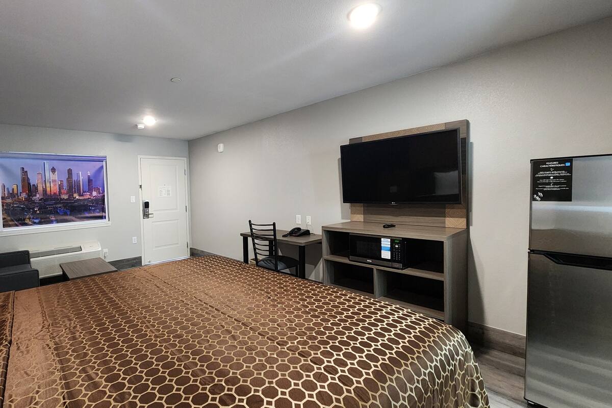 Ein Hotelzimmer mit einem großen Bett, einem Schreibtisch mit Stuhl, einem Fernseher, einer Mikrowelle und einem Kühlschrank.