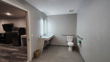 Un baño pequeño con inodoro, lavamanos y barras de apoyo.
