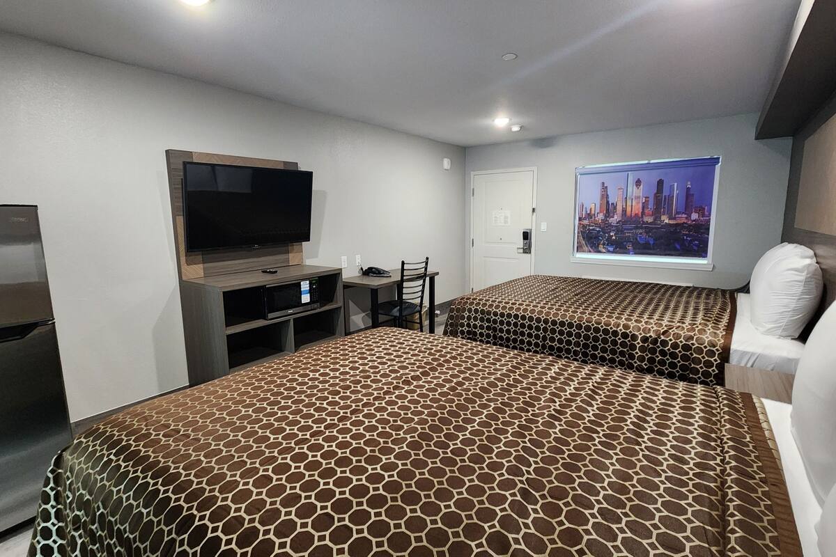 Ein Hotelzimmer mit einem großen Bett, einem Fernseher, einem Schreibtisch und Blick auf die Stadt.