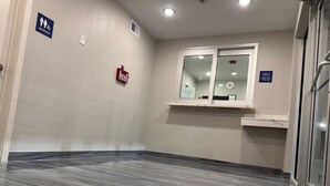 A hotel corridor with a marble floor, a fire alarm, a window with a check-in/check-out sign, and a restroom sign. - Hotel Park Place (Houston)