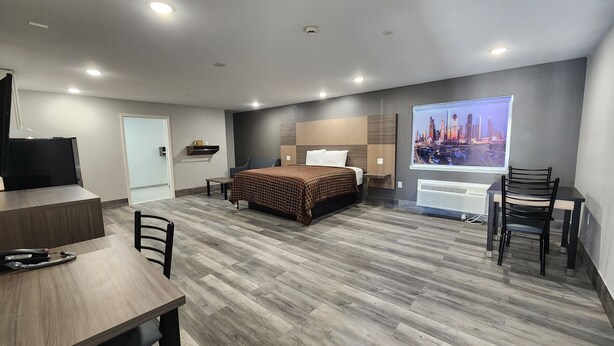 A hotel room with a bed, a desk, a chair, a TV, a window with a cityscape view, and a radiator. - Hotel Park Place (Houston)
