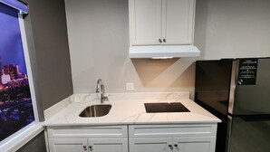 A kitchen with white cabinets, a stainless steel sink, and a black refrigerator. - Hotel Park Place (Houston)