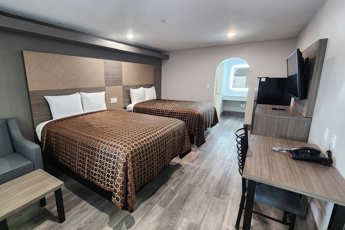 Ein Hotelzimmer mit zwei Betten, einem Sofa, einem Schreibtisch, einem Sessel und einem Fernseher.